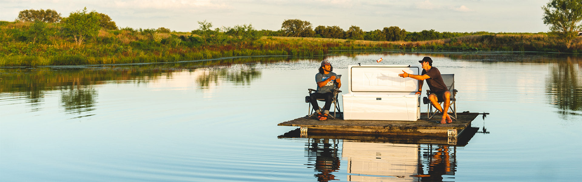 Two people on a pontoon in a calm lake with a scenic background