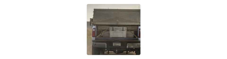 Back of a pickup truck with a cargo bed cover and cooler in a desert setting