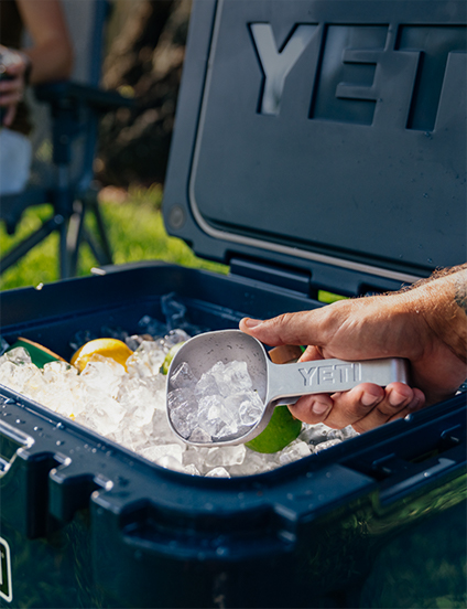 YETI cooler with ice and a scoop, with a person's hand holding the scoop.