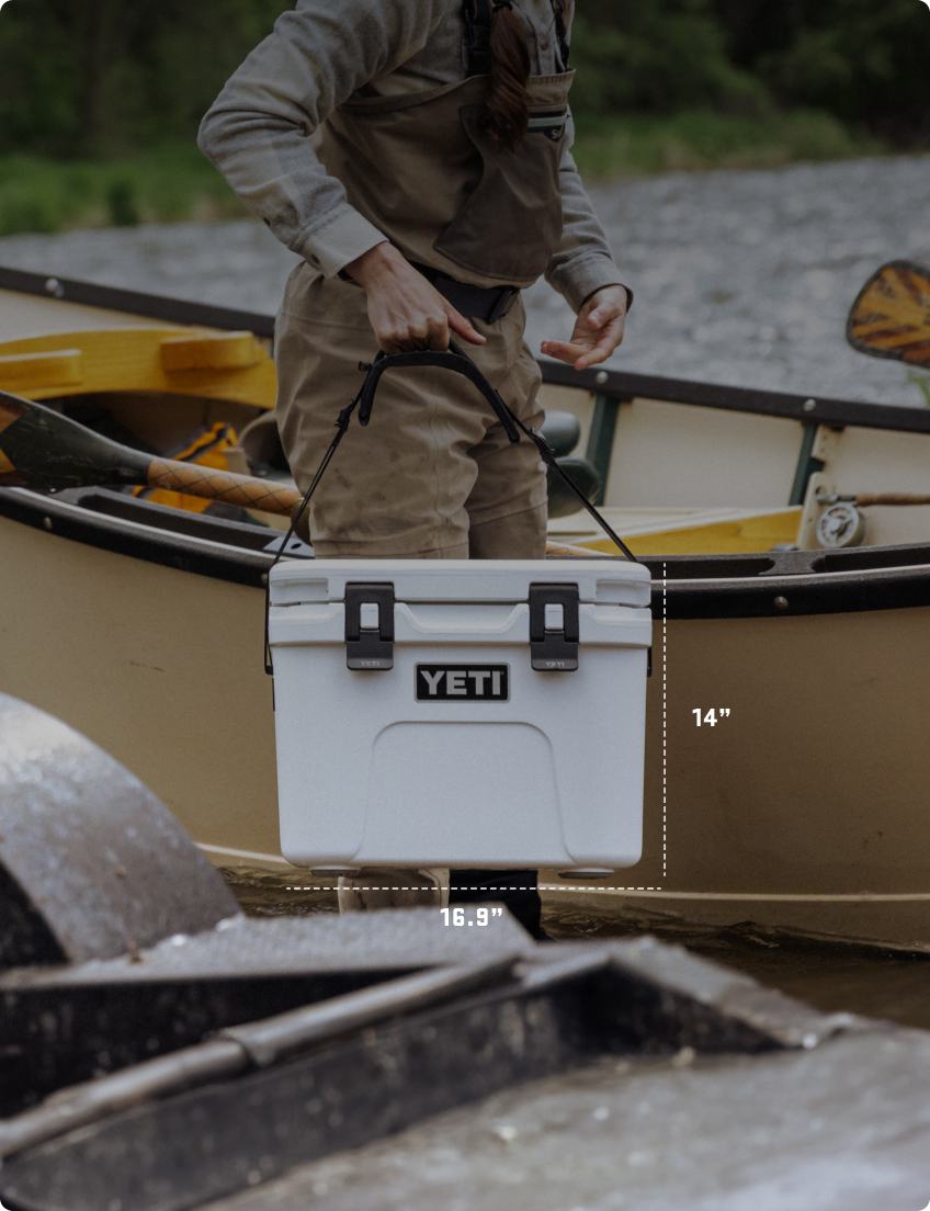 Person holding a YETI cooler with dimensions displayed, near kayaks.