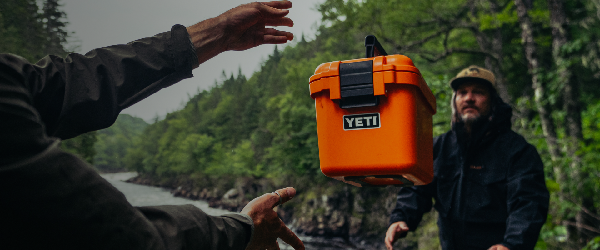 Person holding an orange YETI storage box outdoors with a forest background