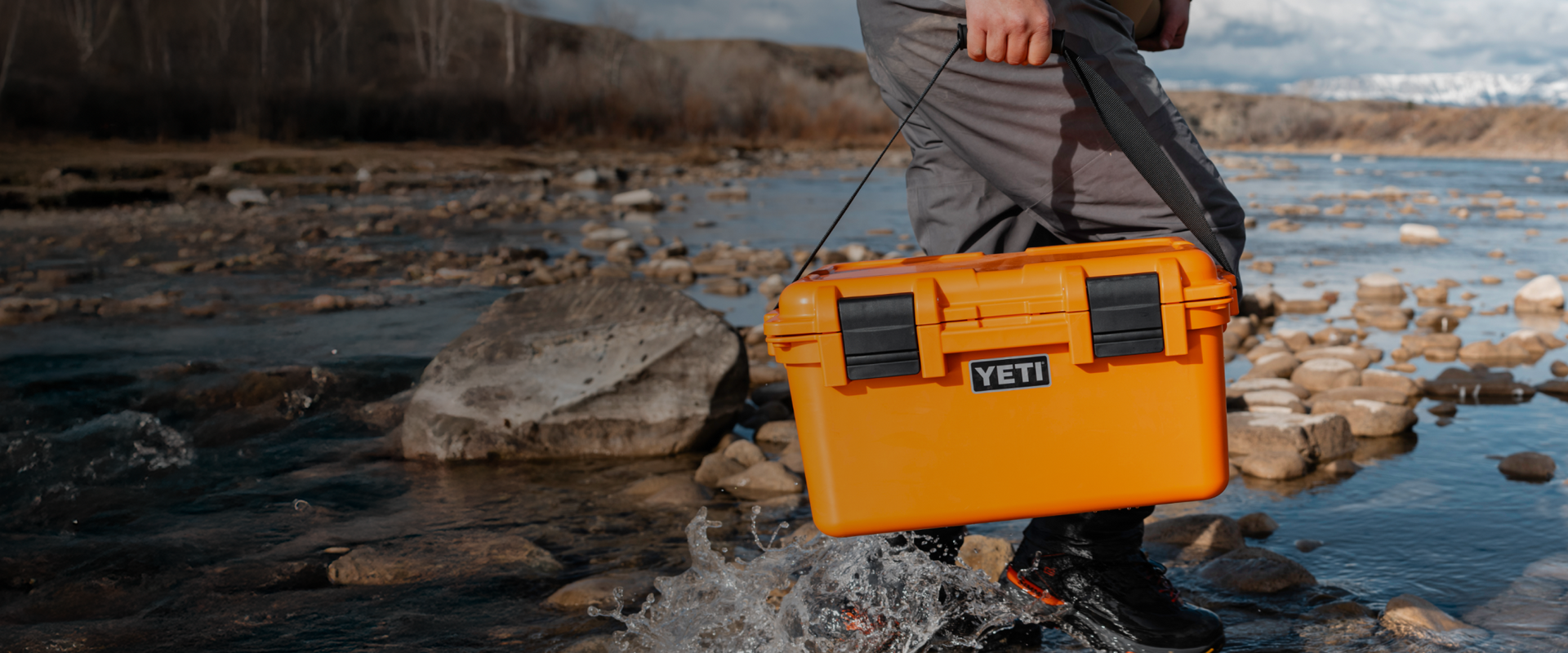 Person holding an orange YETI storage box by a rocky stream