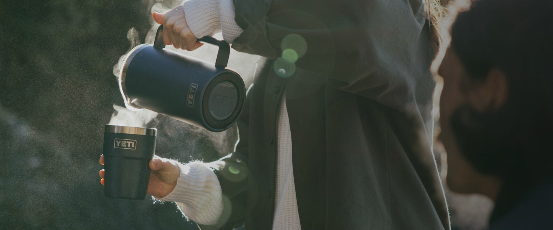 Person holding a Yeti mug outdoors with a blurred background