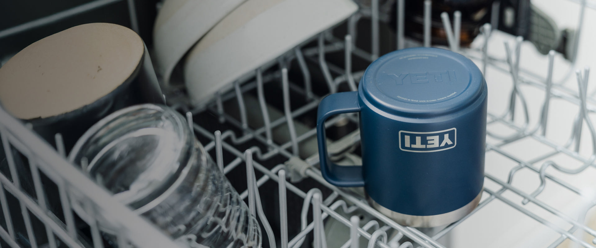 Blue YETI mug in a dishwasher rack with other dishes.