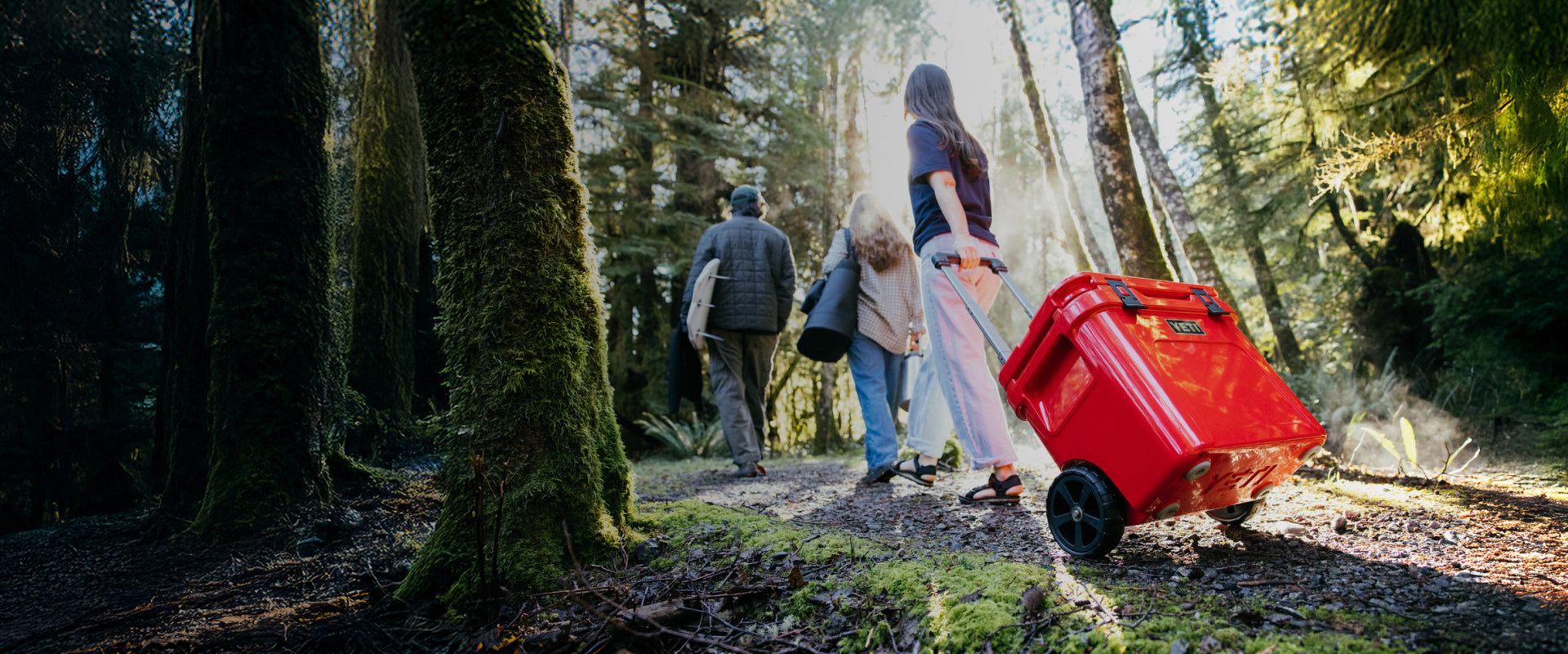 People walking through a forest with a red suitcase