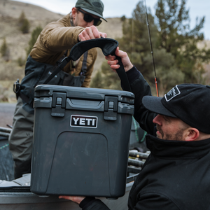 Two men with a YETI cooler outdoors, likely in a mountain or forest setting.