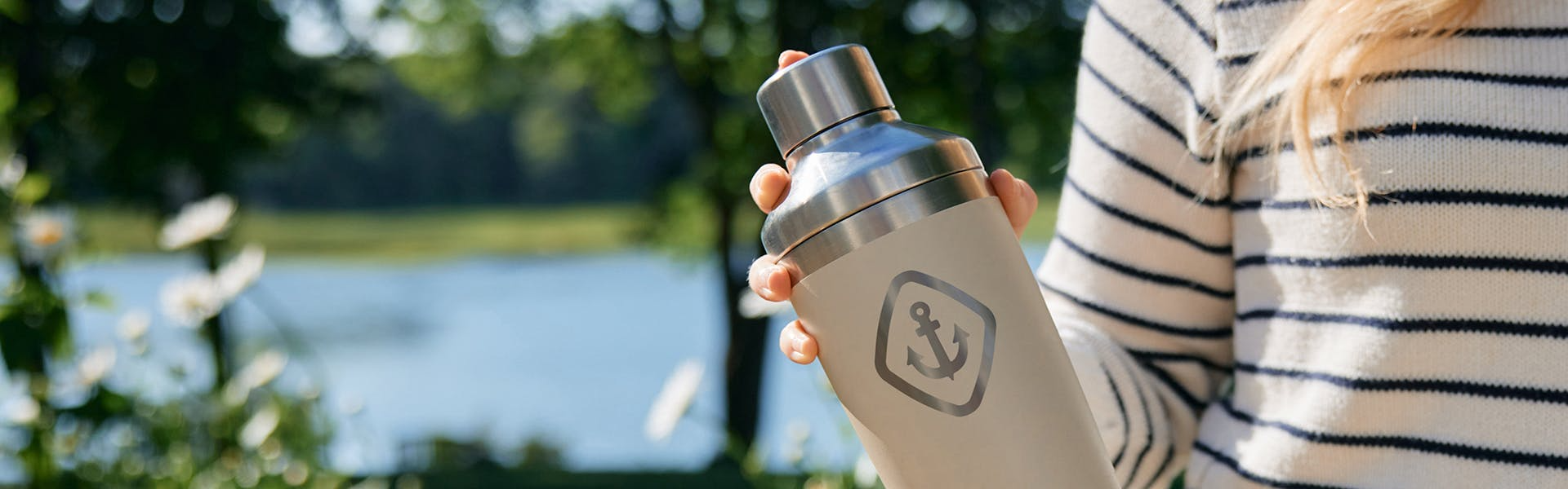 Person holding a beige water bottle with a logo by a lake
