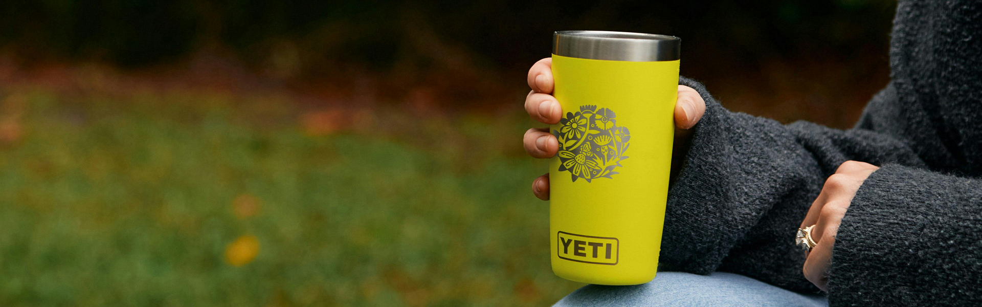 Yellow YETI mug held by a person outdoors with a blurred natural background