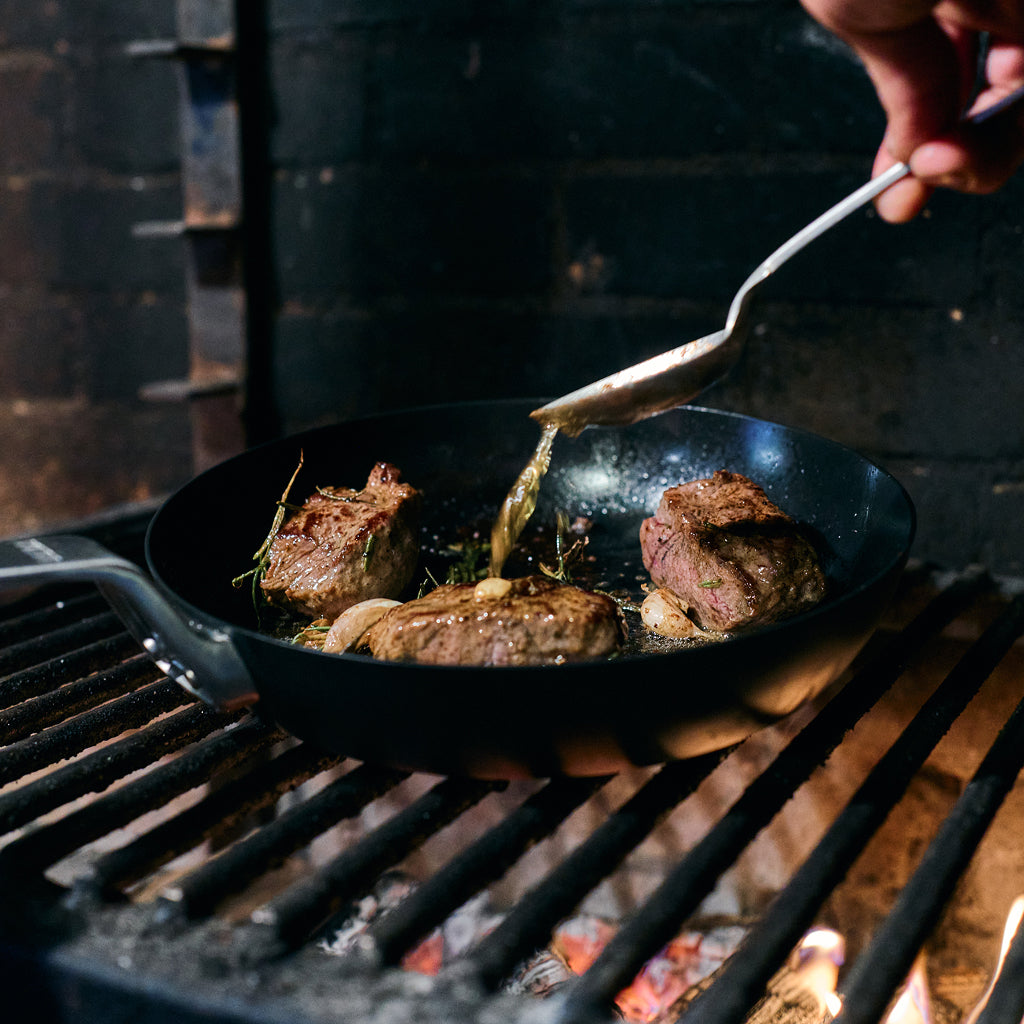 Person cooking steak on a YETI pan over an open fire.