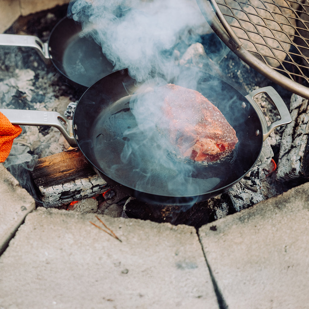 Meat cooking in a YETI frying pan over a campfire