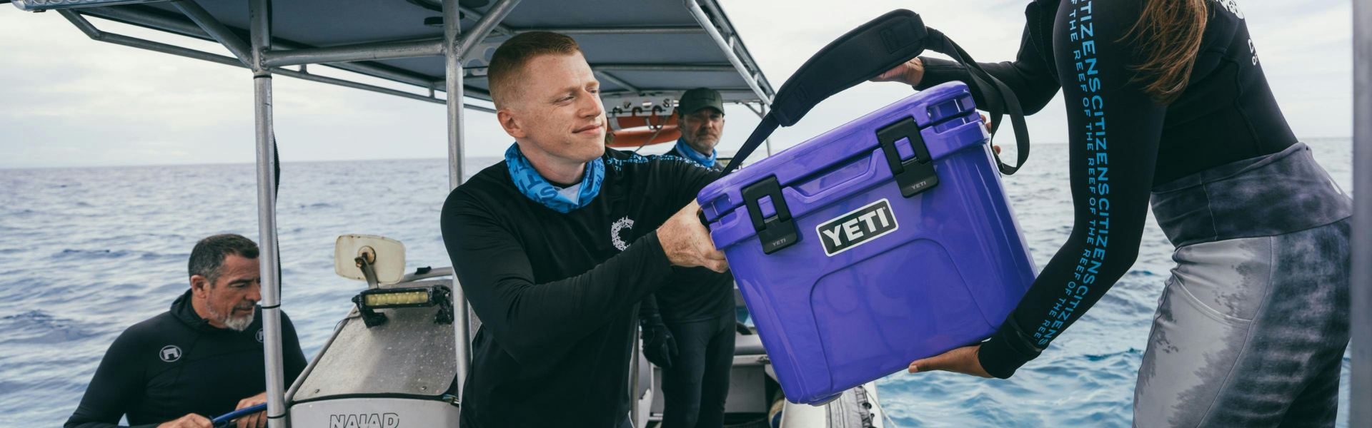 Person holding a purple YETI cooler on a boat with another person in the background.