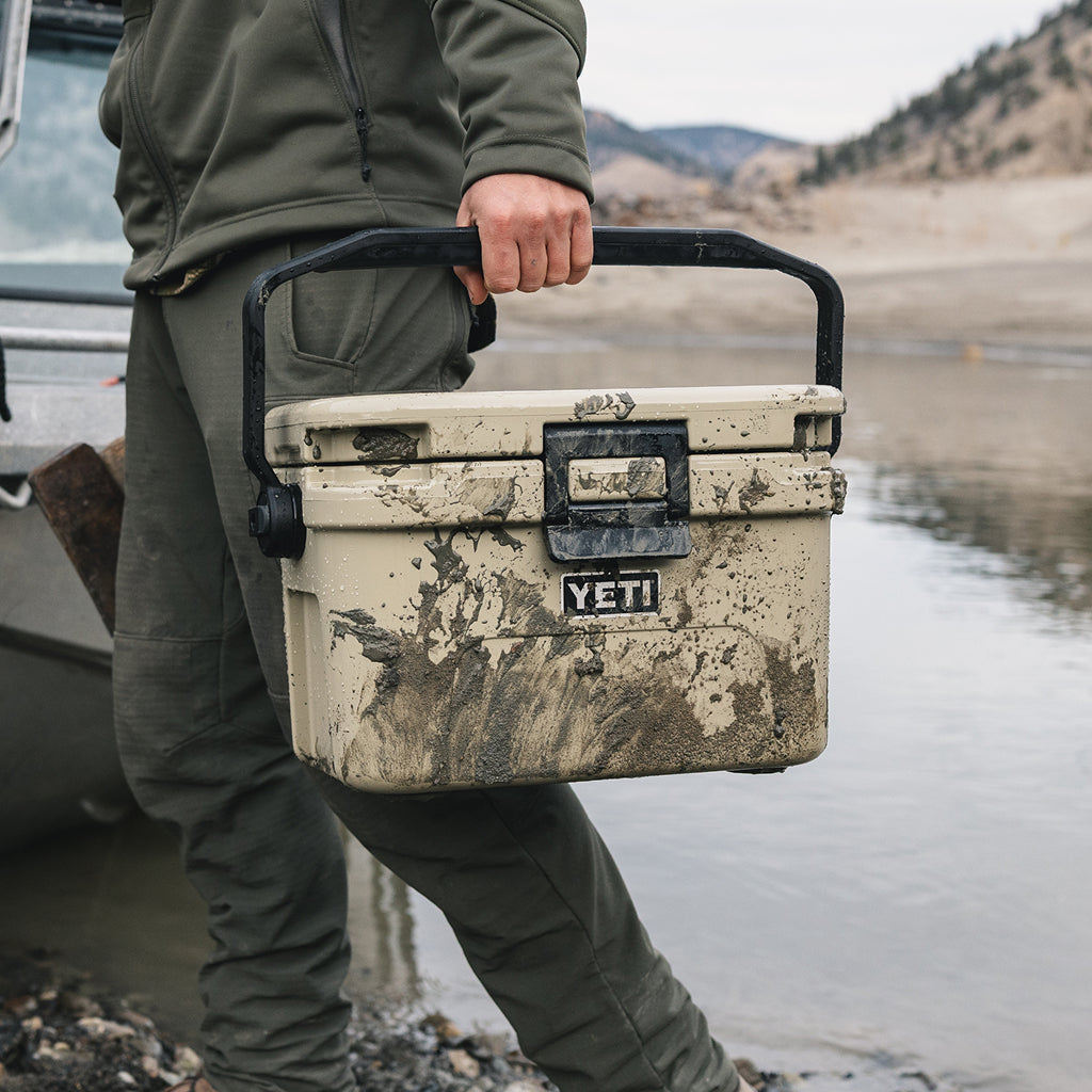 Person holding a YETI cooler by a body of water with mountains in the background