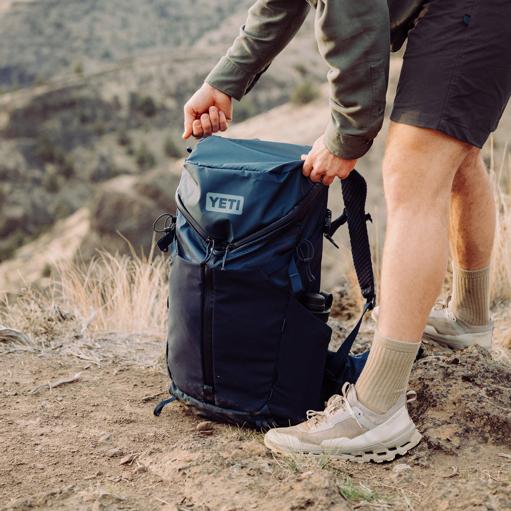 Person holding a YETI backpack in a mountainous landscape
