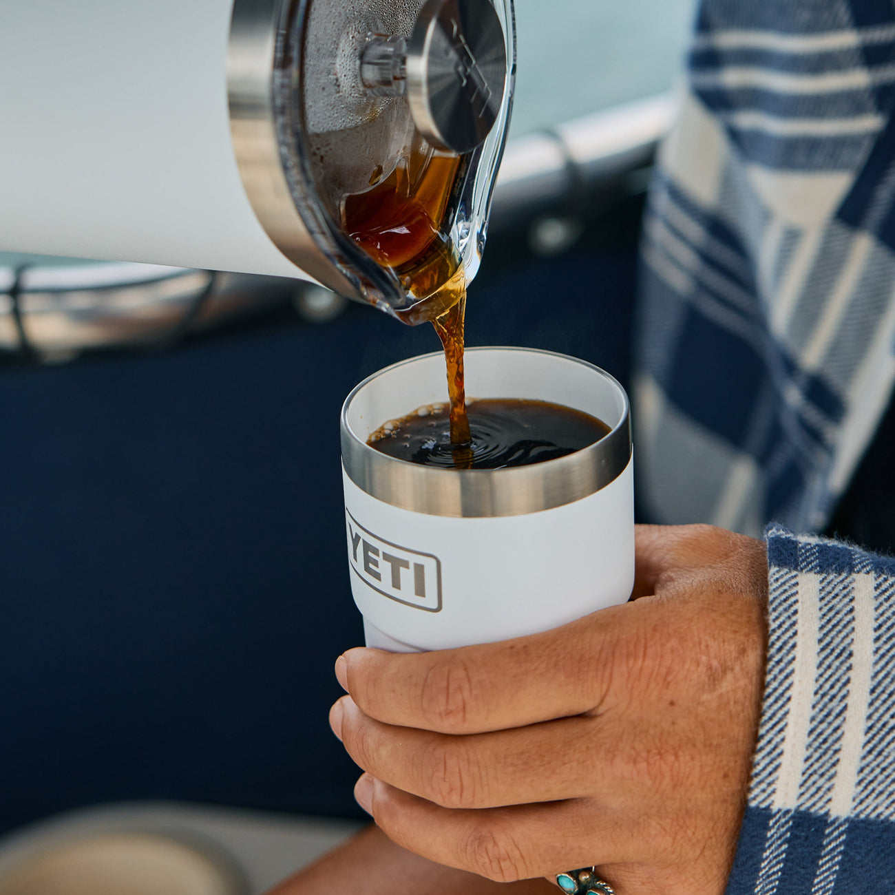 Person pouring coffee into a YETI branded cup outdoors.