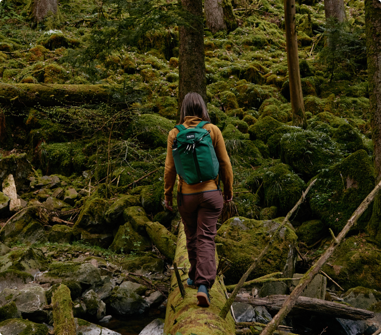 Person with a green backpack walking on a log in a forest
