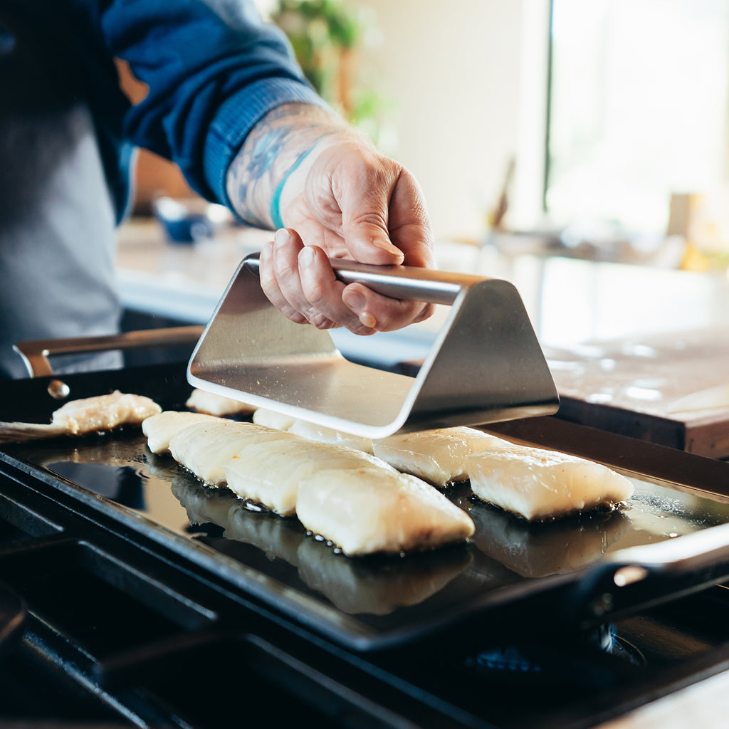 Man using YETI Stainless Steel Grill Press on some fish cooking on a YETI Griddle Pan.