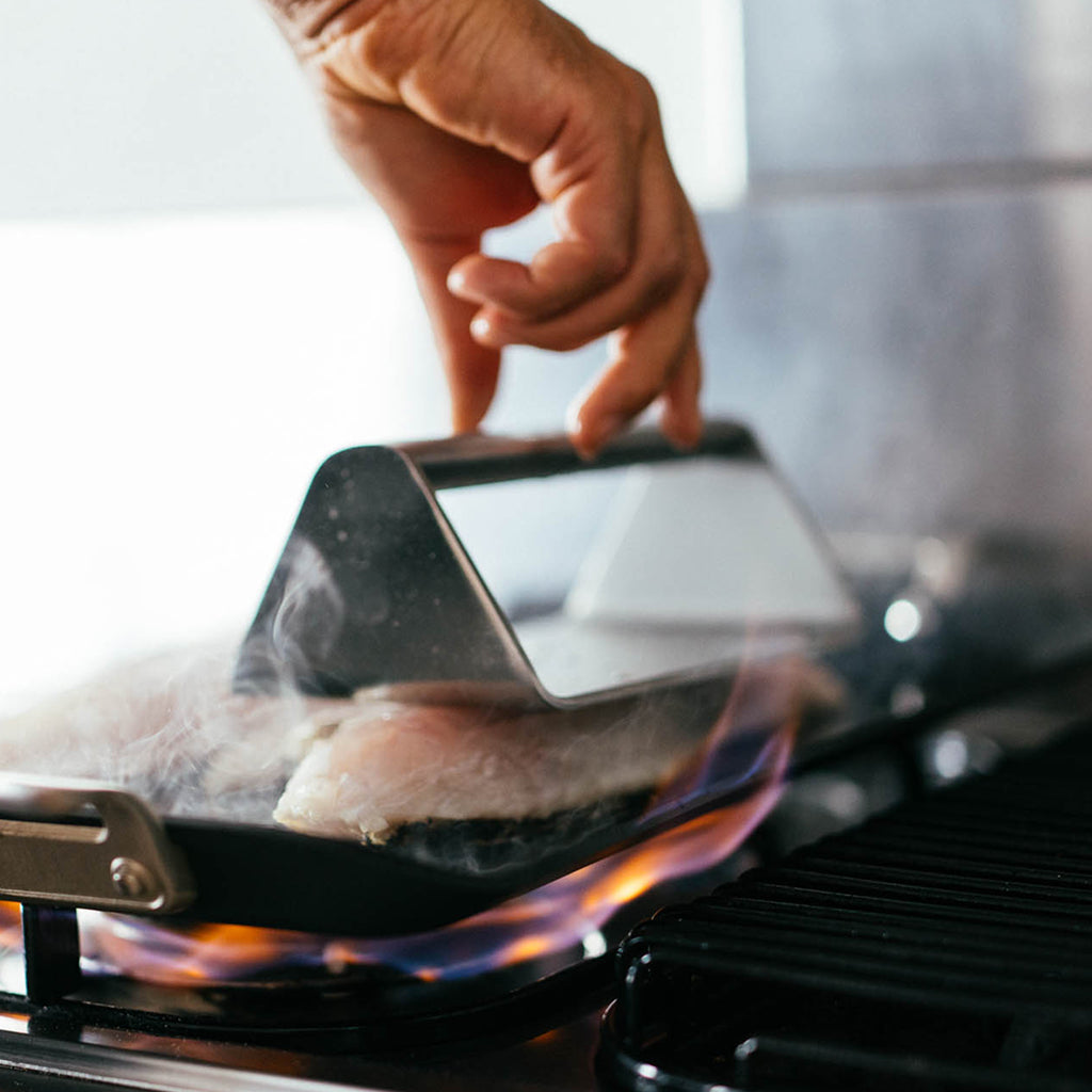 A YETI grill press being used on a piece of fish cooking on a griddle.