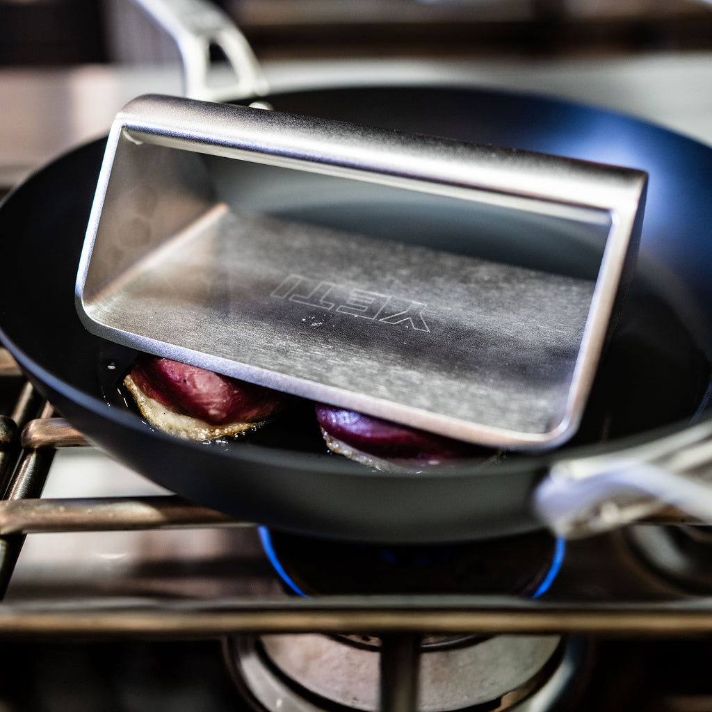 YETI grill press being used in a carbon steel pan