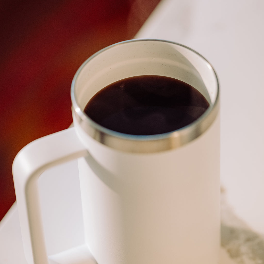 White mug filled with dark liquid on a blurred background