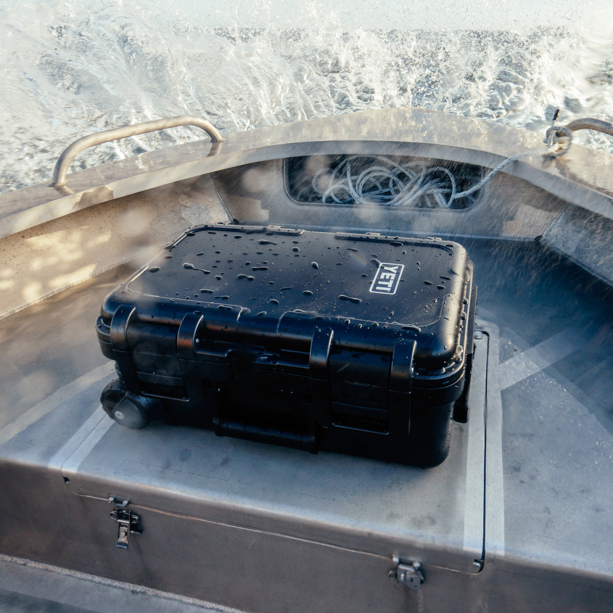 A black YETI hard case with wheels sits inside a boat cabin, covered in water droplets. The YETI logo is visible on the top right of the case.