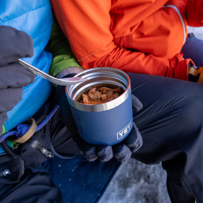 Person holding a blue Yeti insulated mug with food in a snowy setting