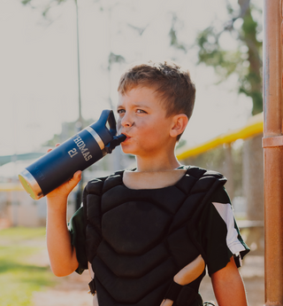 Child in protective gear drinking from a blue water bottle outdoors