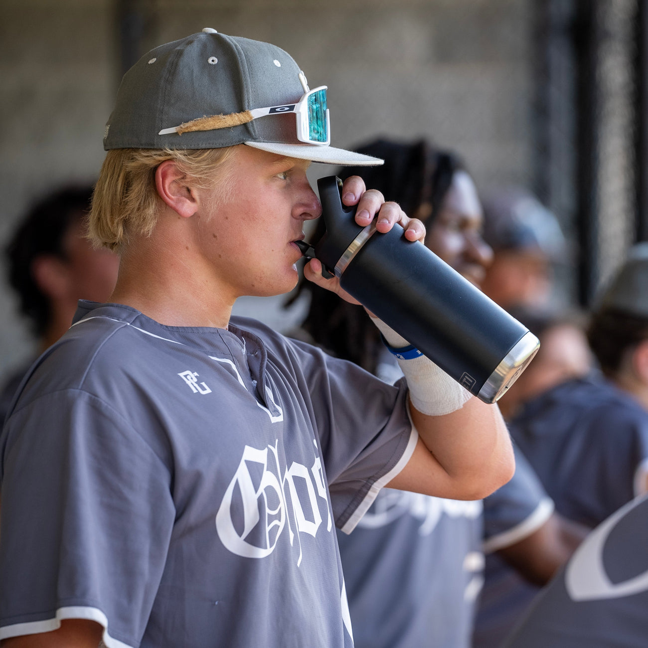 Person in a sports jersey drinking from a black YETI bottle with a straw in a blurred background