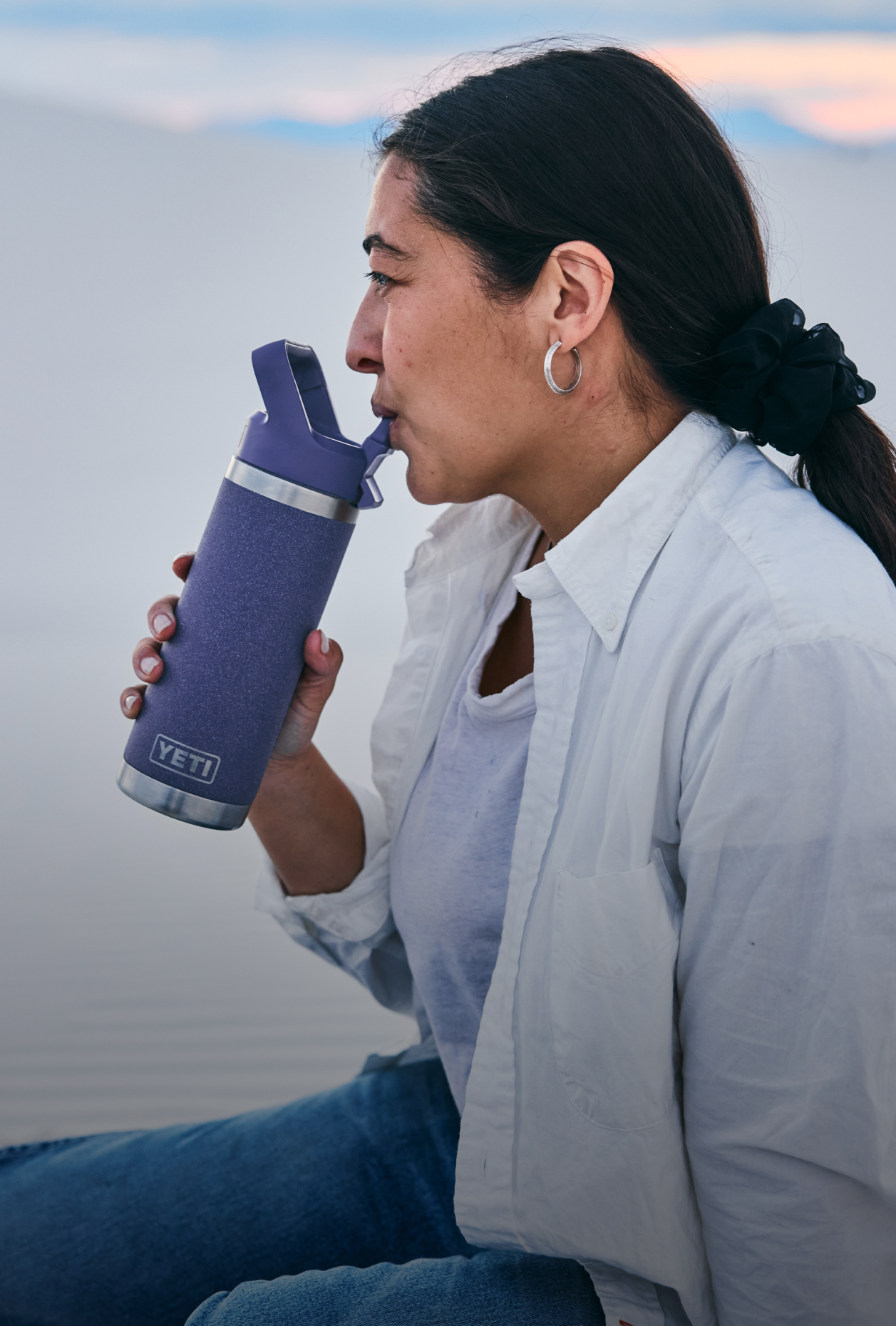 Person drinking from a purple YETI water bottle outdoors