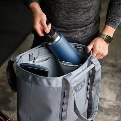 Person holding a grey tote bag with a blue water bottle inside, on a blurred background
