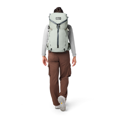 Person wearing a large backpack with 'YETI' branding on a white background