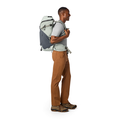 Man wearing a gray backpack and brown pants on a white background