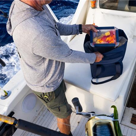 Person on a boat holding a cooler with fishing gear