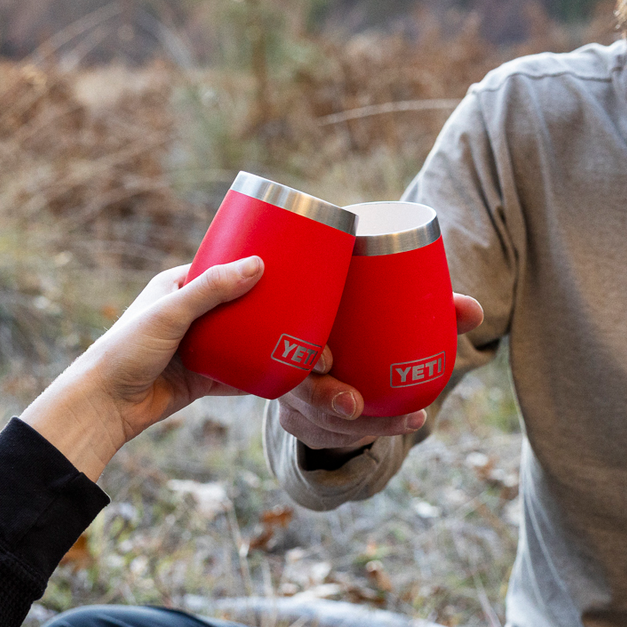 Two red YETI wine tumblers being held in a outdoor setting.