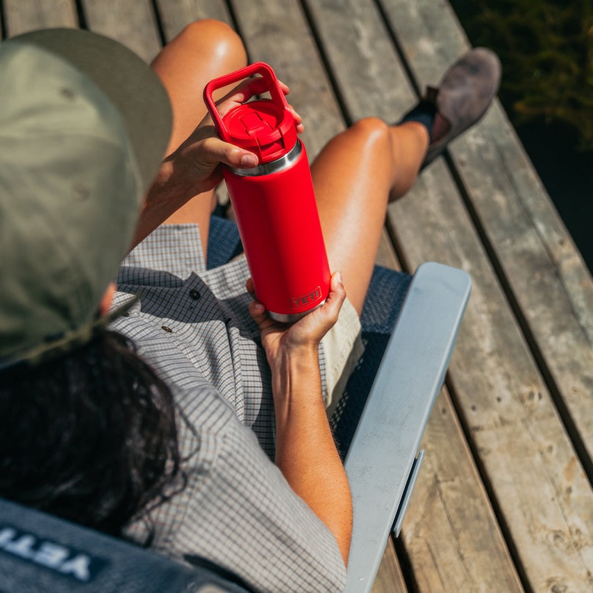 Person sitting on a wooden dock holding a red YETI water bottle.