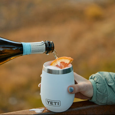 Person pouring sparkling wine into a YETI insulated wine tumbler outdoors.